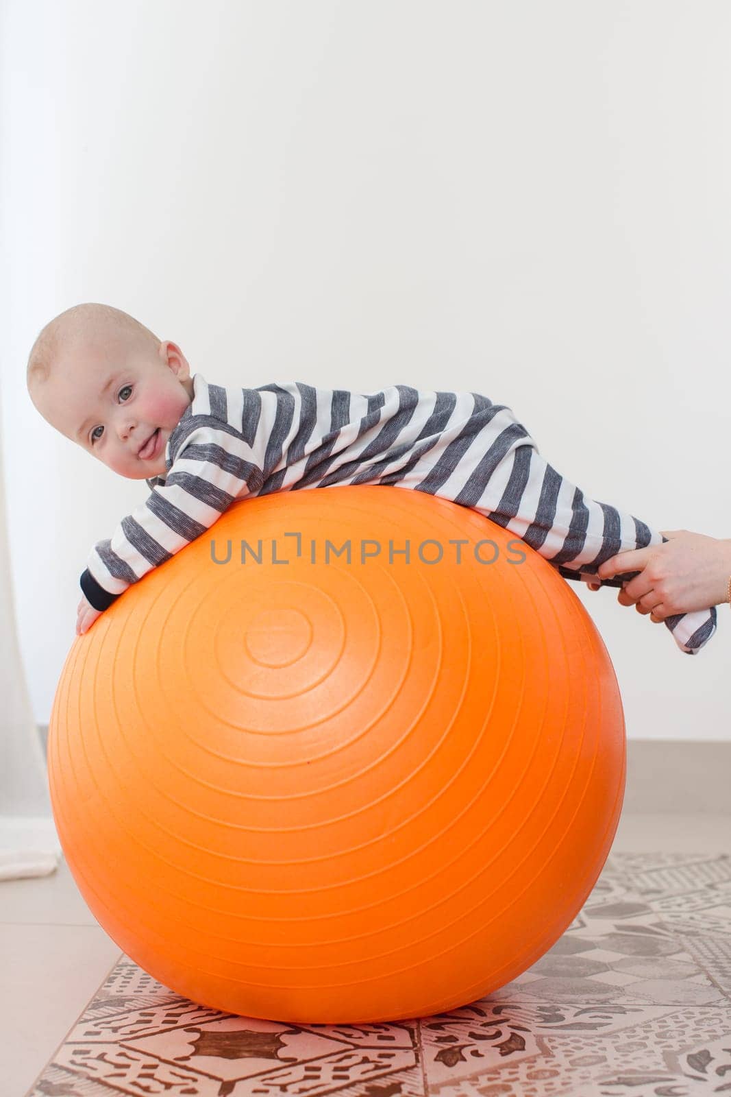 A little boy with tongue out lying on a fitball. Vertical studio shot.