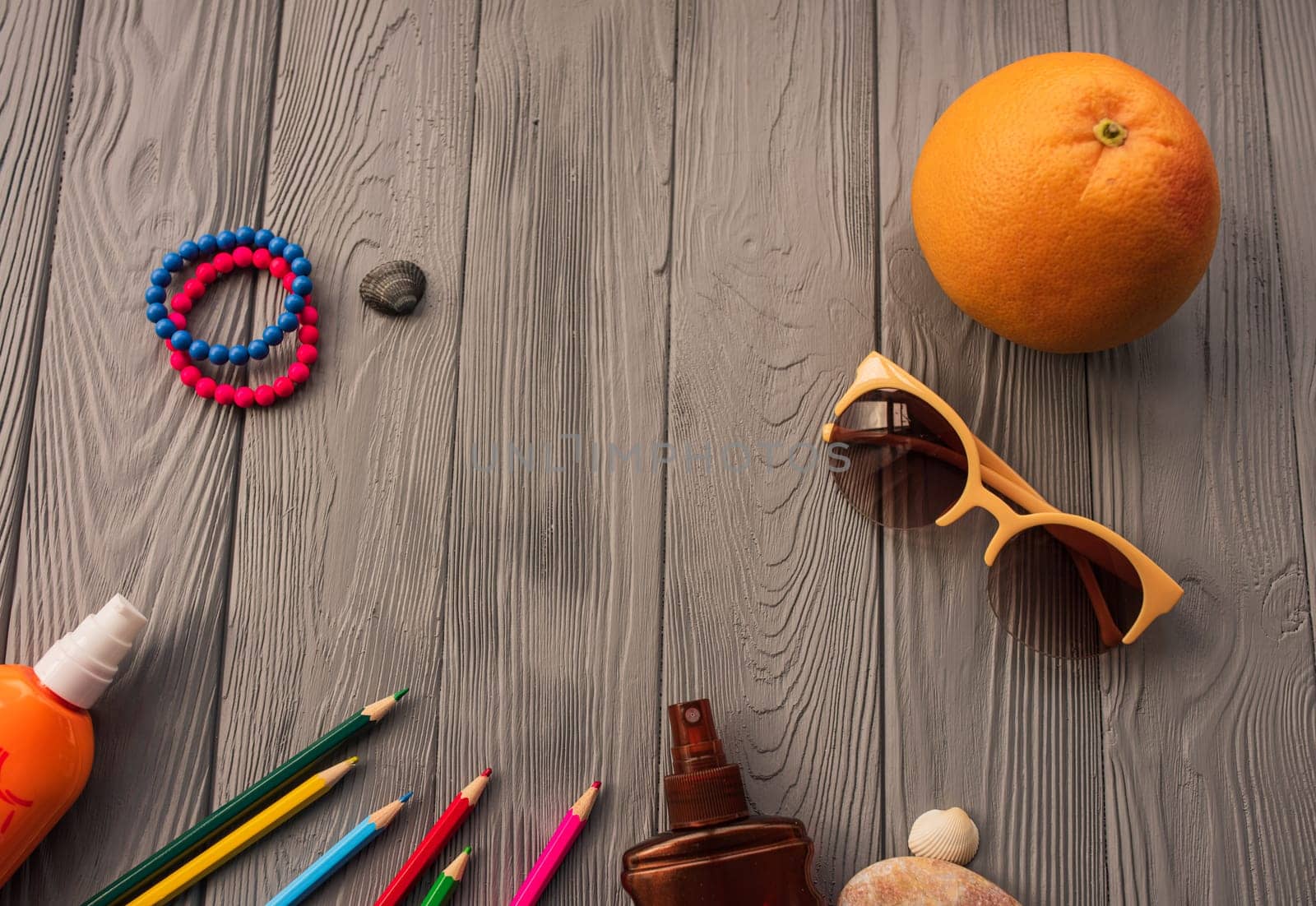 artist pencils for inscription. accessories sunscreen spf care. sunglasses bracelets orange fruit pebbles. Summer background template mockup space colorful composition text. Top view wooden background