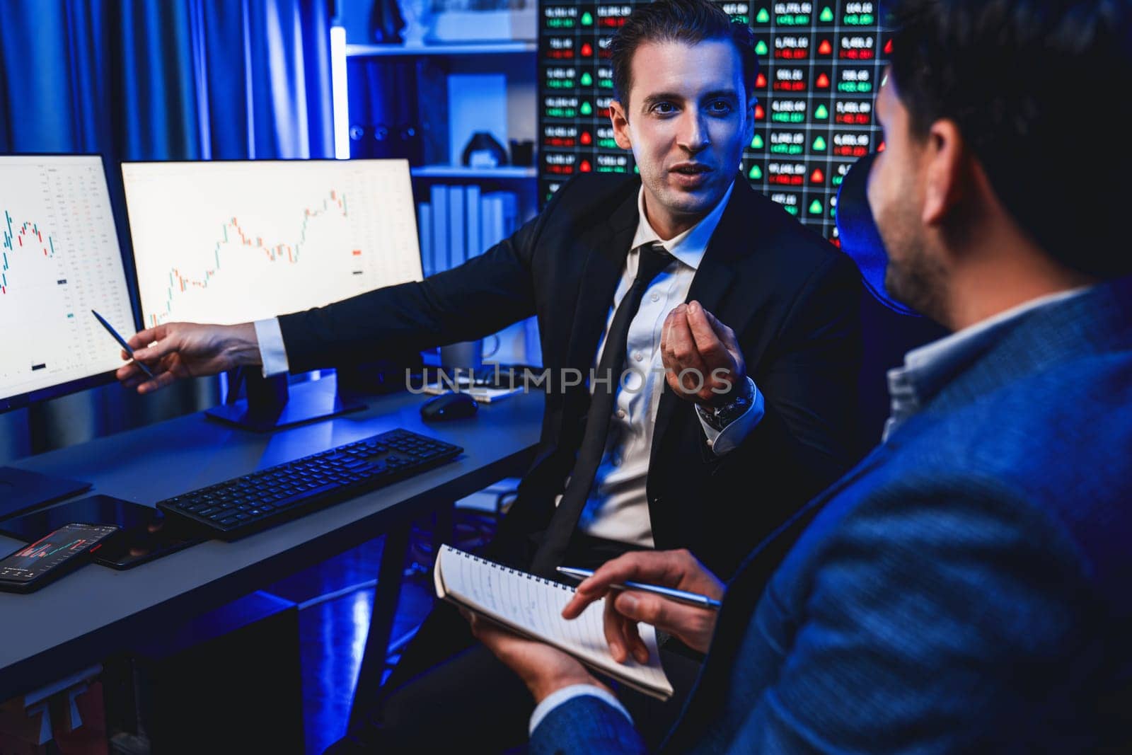 Two stock exchange traders discussing on dynamic investment graph, trending of high profit in currency stock. Showing financial benefit data on monitor screen in neon light at workplace. Sellable.