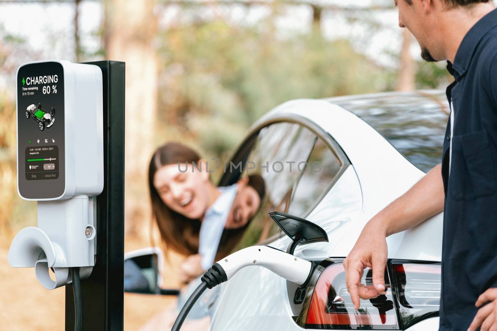 Lovely young couple recharging battery for electric car during autumnal road trip travel EV car in autumnal forest. Eco friendly travel on vacation during autumn. Exalt