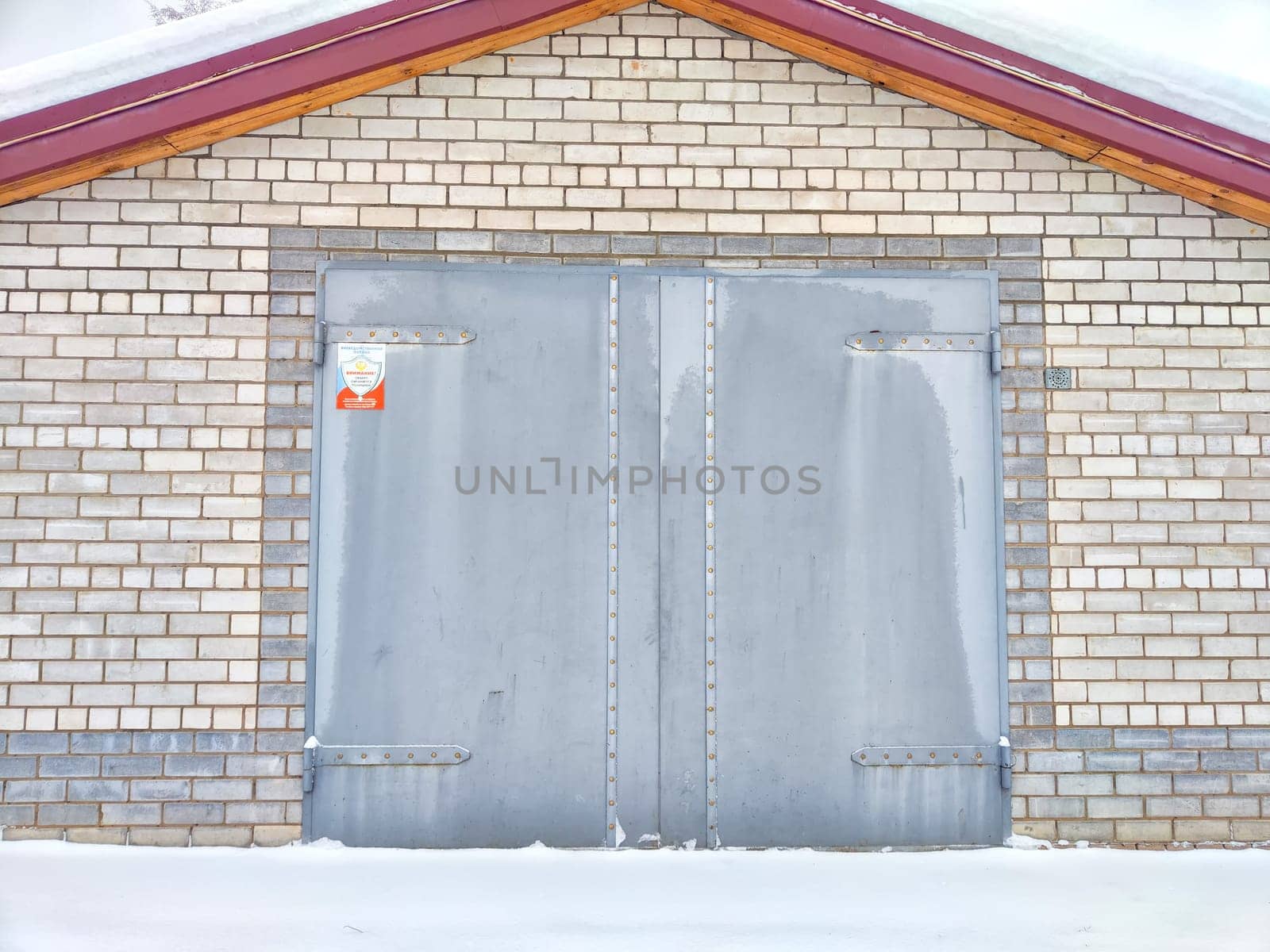 closed iron gate on a gray brick wall of a garage outside in white snow