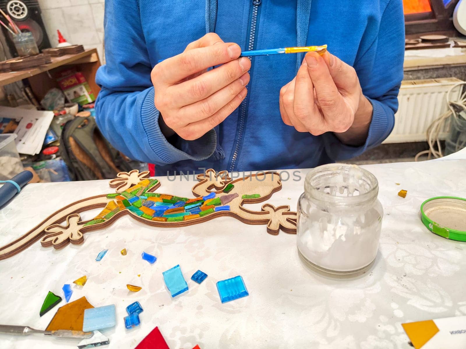 Kazan, Russia - February 23, 2024: An artist trims tiles for colorful mosaic. Crafting a Mosaic Artwork at a Workshop Table