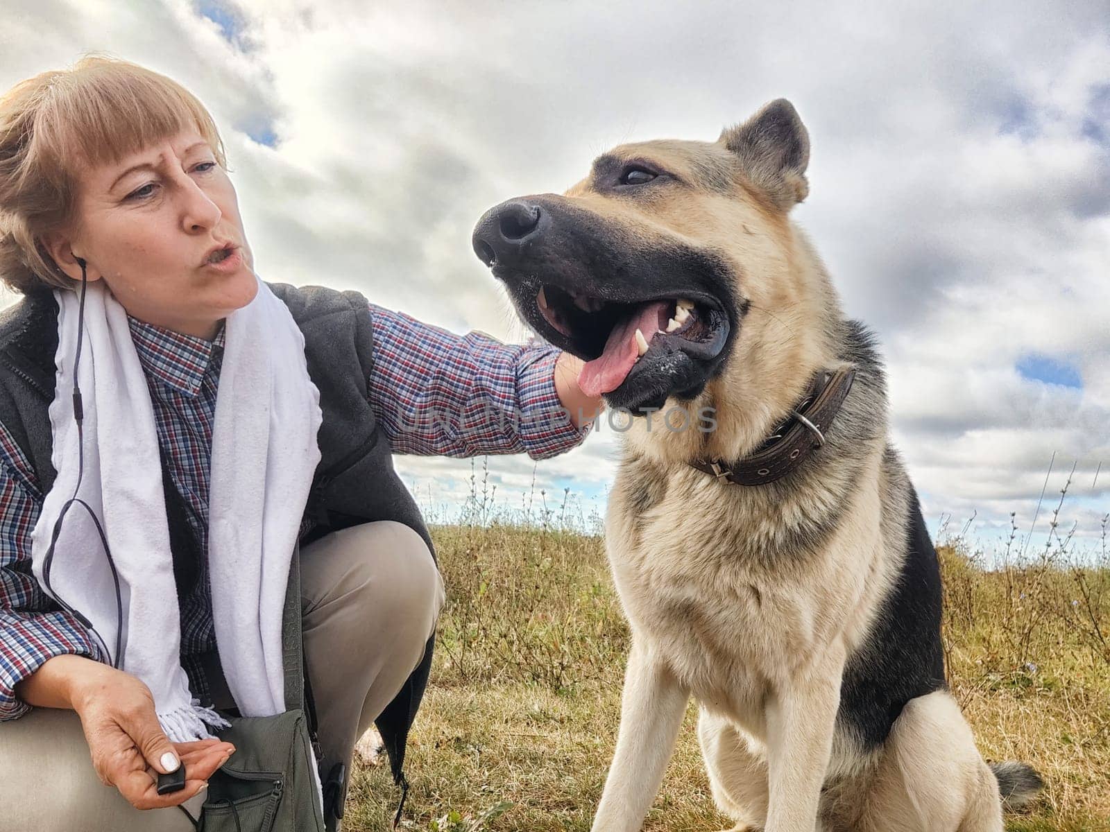 Adult girl with shepherd dog taking selfies in field. Middle aged woman and big shepherd dog on nature. Friendship, love, communication, fun, hugs