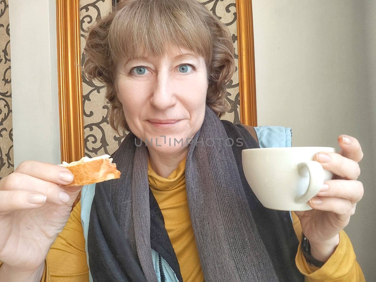 Mature Woman Enjoying Light Breakfast With Coffee by the Window. Woman in with morning coffee and bread. A blogger takes selfie while eating