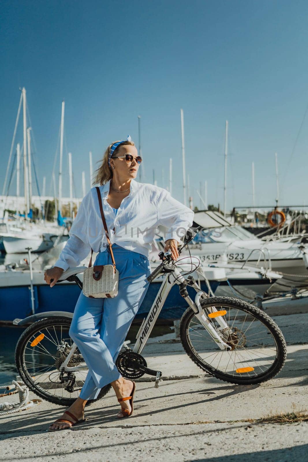 Woman enjoys bike ride along waterfront, Marina surroundings. She is wearing a white shirt and blue jeans, and she has a handbag with her. Capturing outdoor bike ride by waterfront