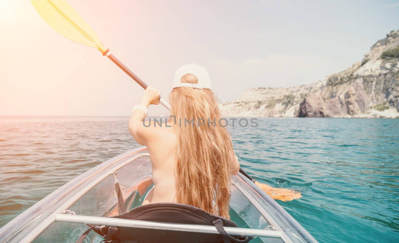 Woman in kayak back view. Happy young woman with long hair floating in transparent kayak on the crystal clear sea. Summer holiday vacation and cheerful female people relaxing having fun on the boat by panophotograph