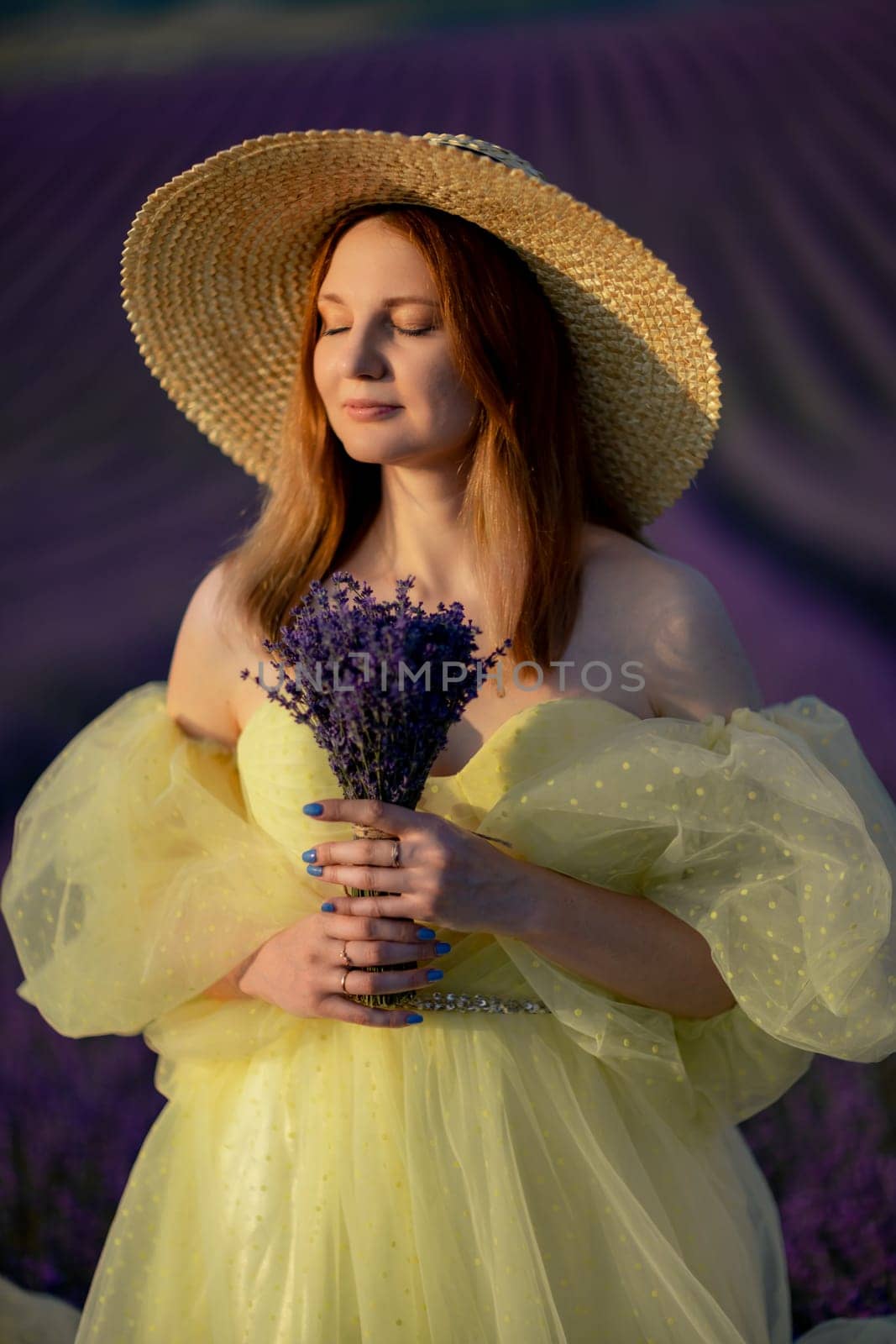 Lavender sunset girl. A laughing girl in a blue dress with flowing hair in a hat walks through a lilac field, holds a bouquet of lavender in her hands