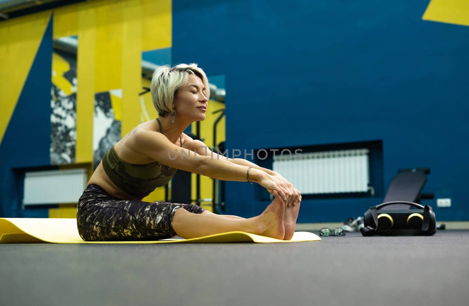 a slender athletic woman in the gym is beautifully engaged in yoga exercises on a mat by Rotozey