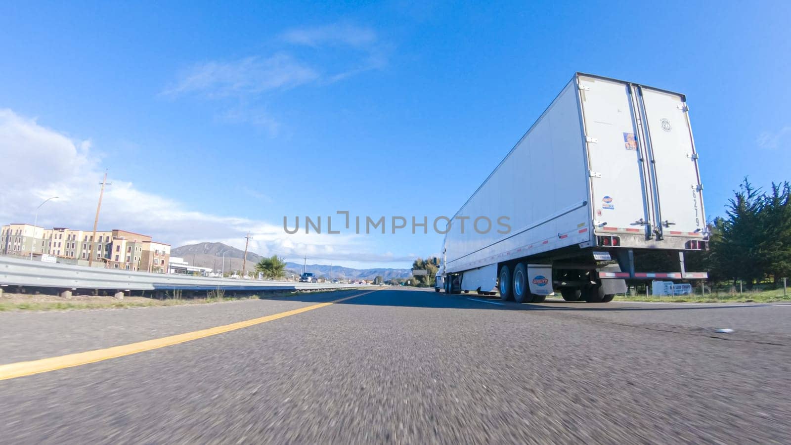 Santa Maria, California, USA-December 6, 2022-On a crisp winter day, a car cruises along the iconic Highway 1 near San Luis Obispo, California. The surrounding landscape is brownish and subdued, with rolling hills and patches of coastal vegetation flanking the winding road.