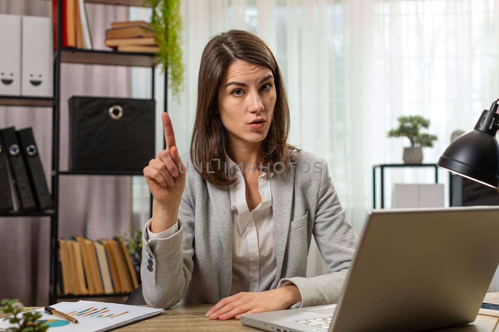 Young businesswoman working on laptop computer shakes finger and saying no be careful scolding and giving advice to avoid danger mistake disapproval sign at home office. Confident freelancer girl.