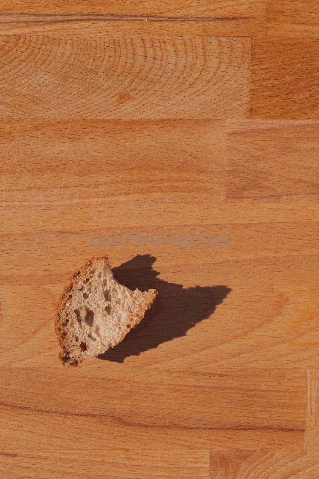 A single slice of bread casting a shadow on a wooden surface