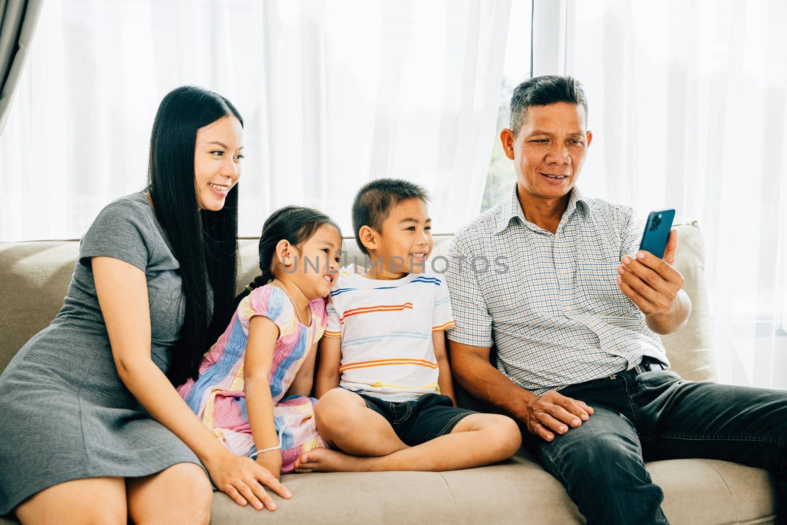 A happy family gathers on a couch kids entertained with a smartphone video parents and children enjoying mobile apps. Illustrating familial joy bonding and technology's role in shared happiness.