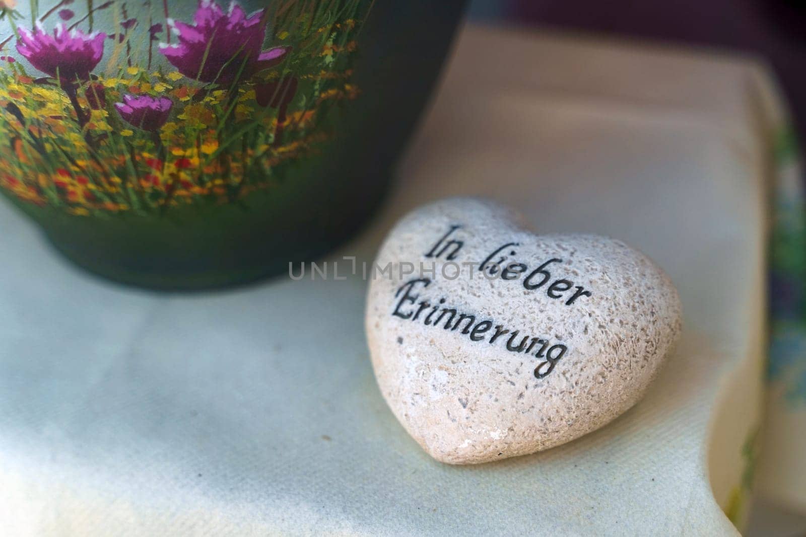 A heart-shaped rock lies next to a vase filled with colorful flowers, creating a sweet and natural arrangement. There is an inscription on the stone in German - In lovely memories