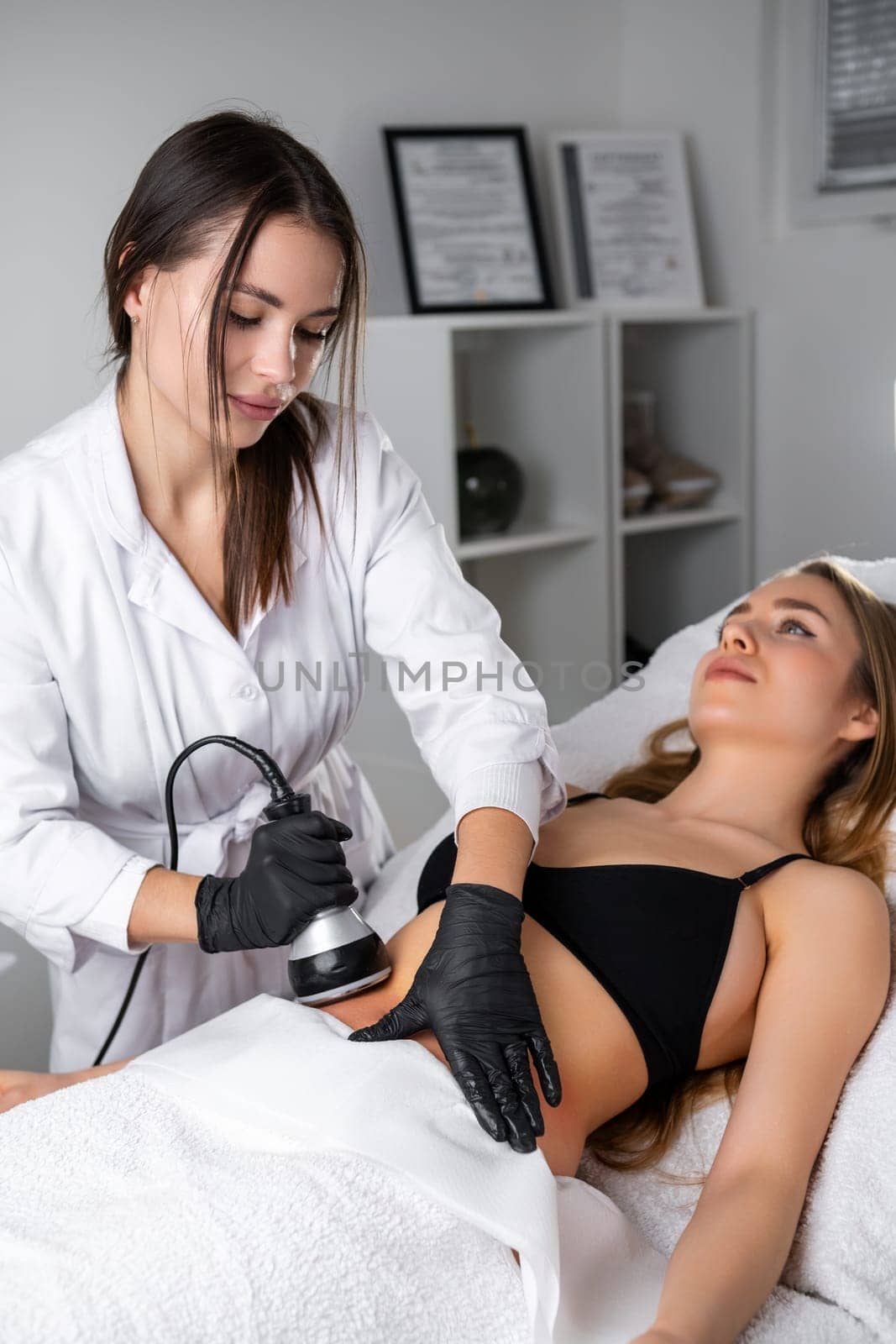 Portrait of young cosmetologist doing cavitation procedure to young patient by vladimka