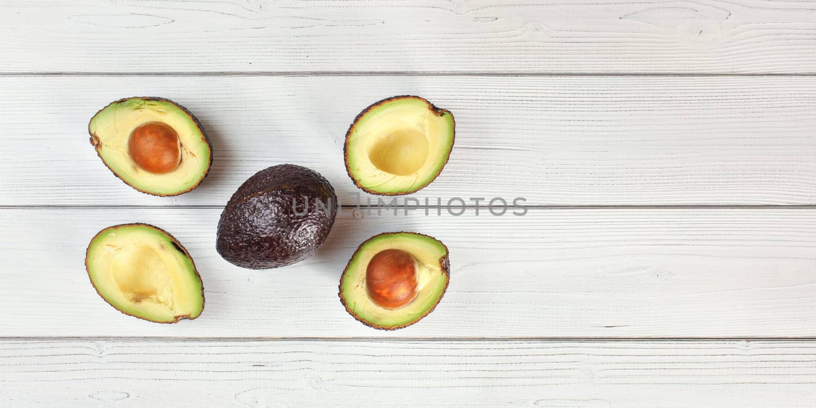 Ripe brown avocado - Hass bilse variety - halved and arranged on white boards desk, view from above, space for text right side by Ivanko