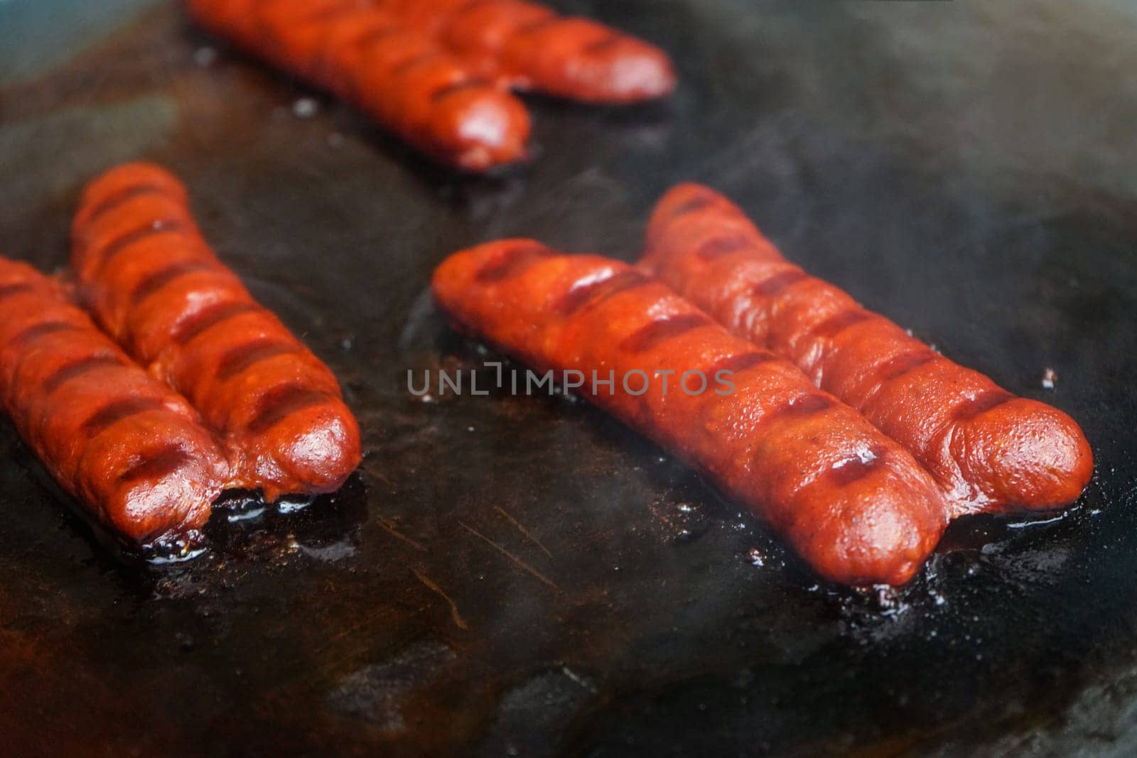 Small bratwurst / hot dog frankfurter sausages grilled on electric grill, smoke visible above