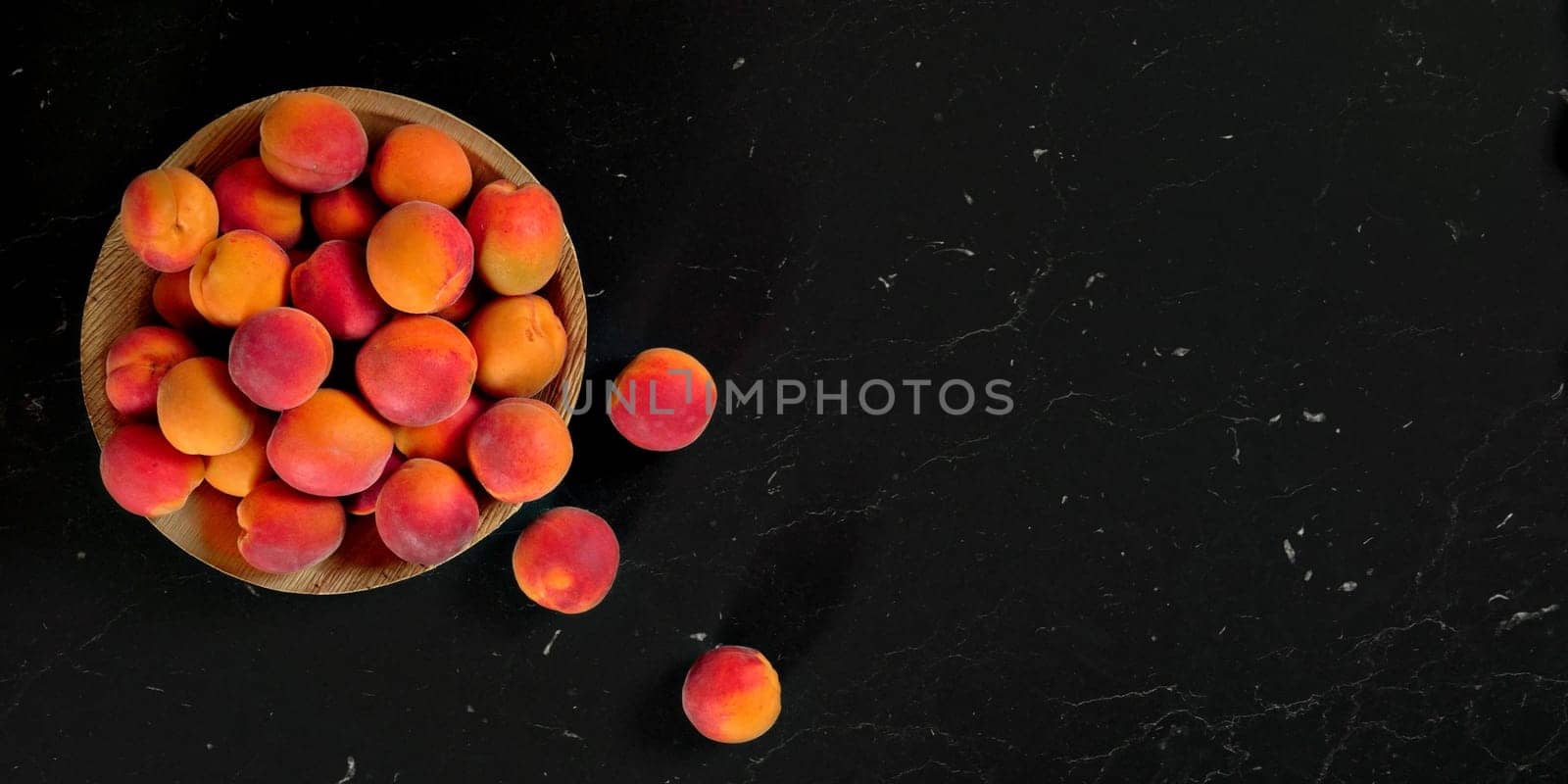 Small bowl with apricots, some of them scattered near on black marble like table - view from above, space for text right side by Ivanko