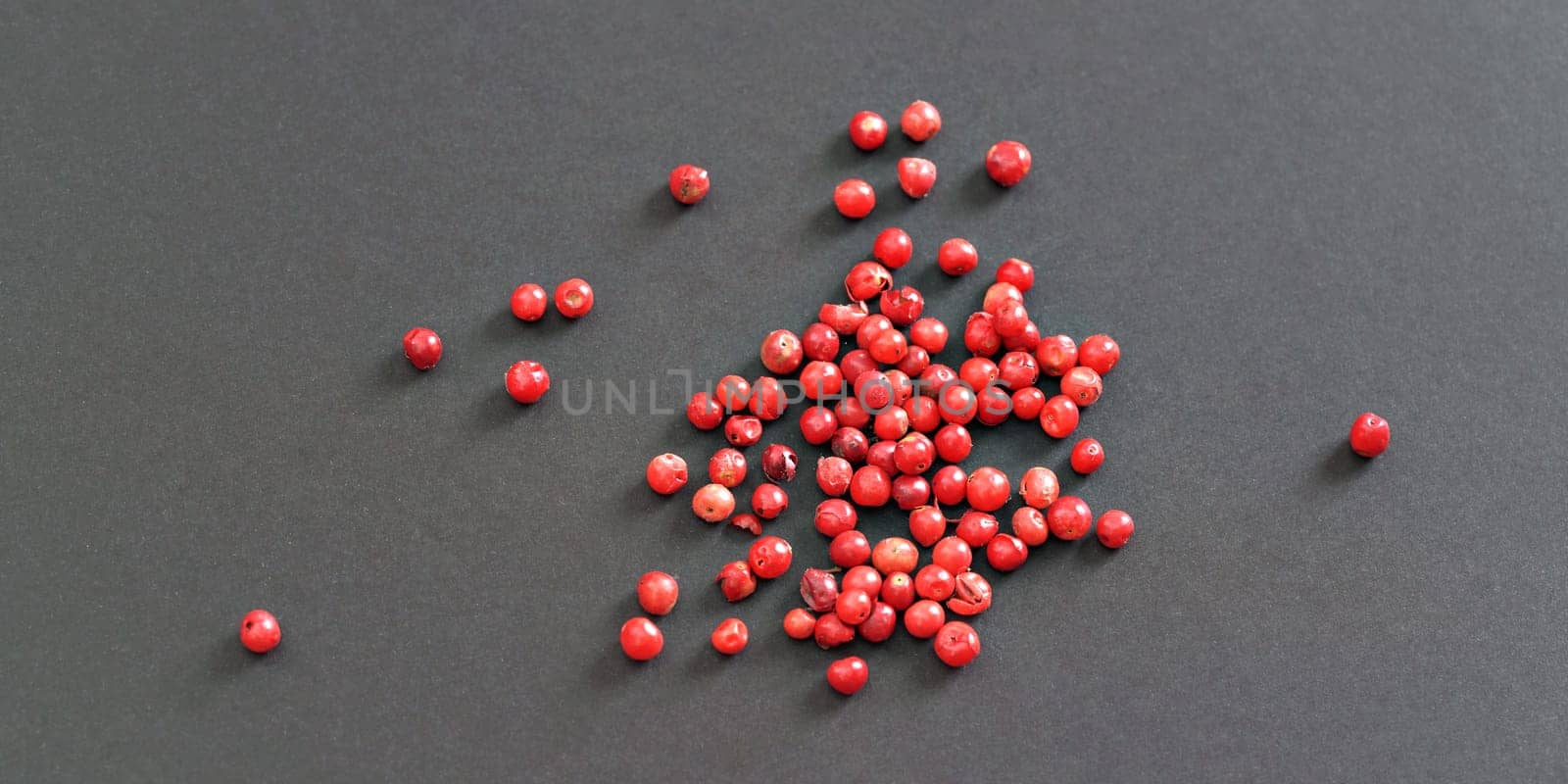 Whole pink / red peppercorns on black / gray paper, view from above by Ivanko