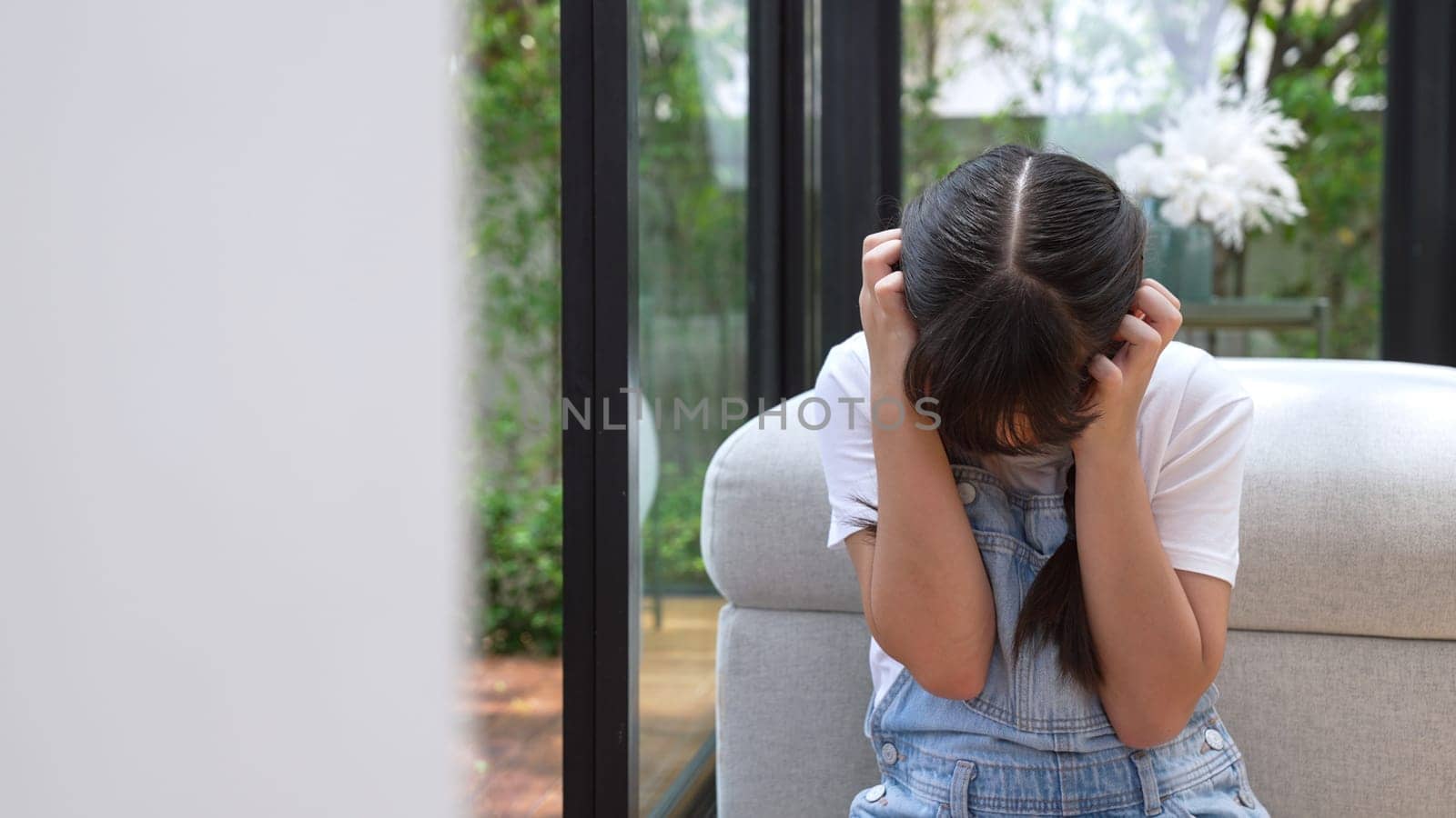 Stressed and unhappy young girl huddle in corner, cover her ears blocking sound of her parent arguing in background. Domestic violence at home and traumatic childhood develop to depression. Synchronos