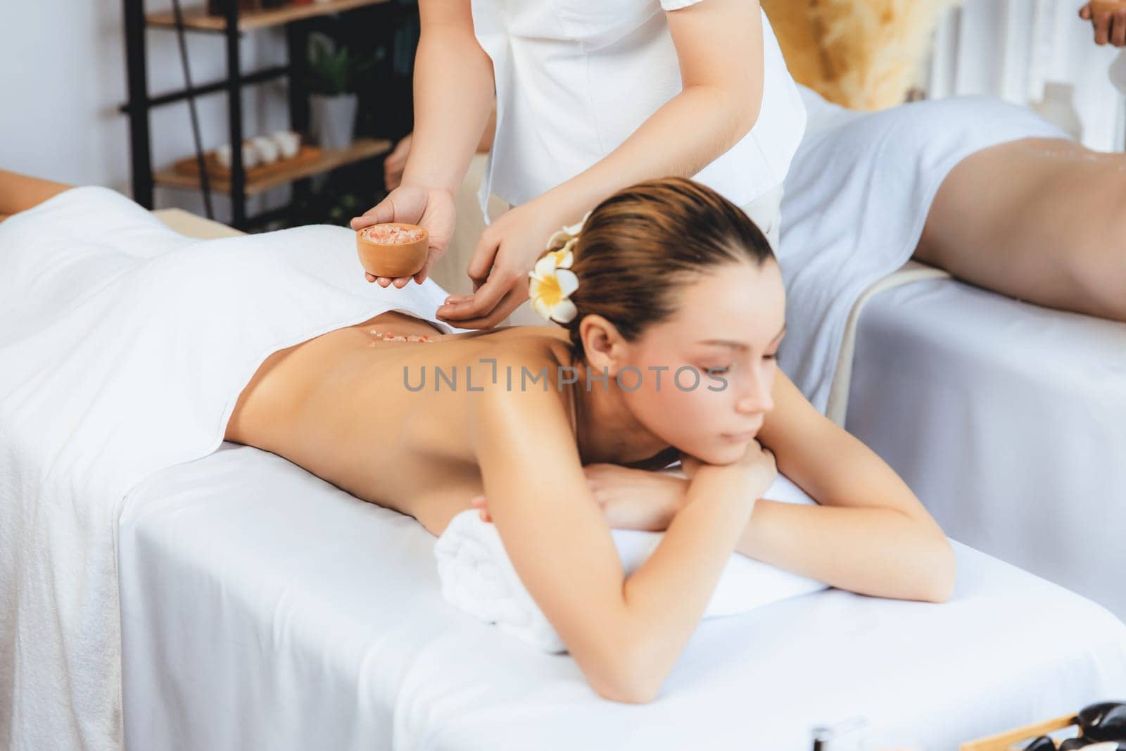 Blissful couple customer having exfoliation treatment in luxury spa salon with warmth candle light ambient. Salt scrub beauty treatment in health spa body scrub. Quiescent