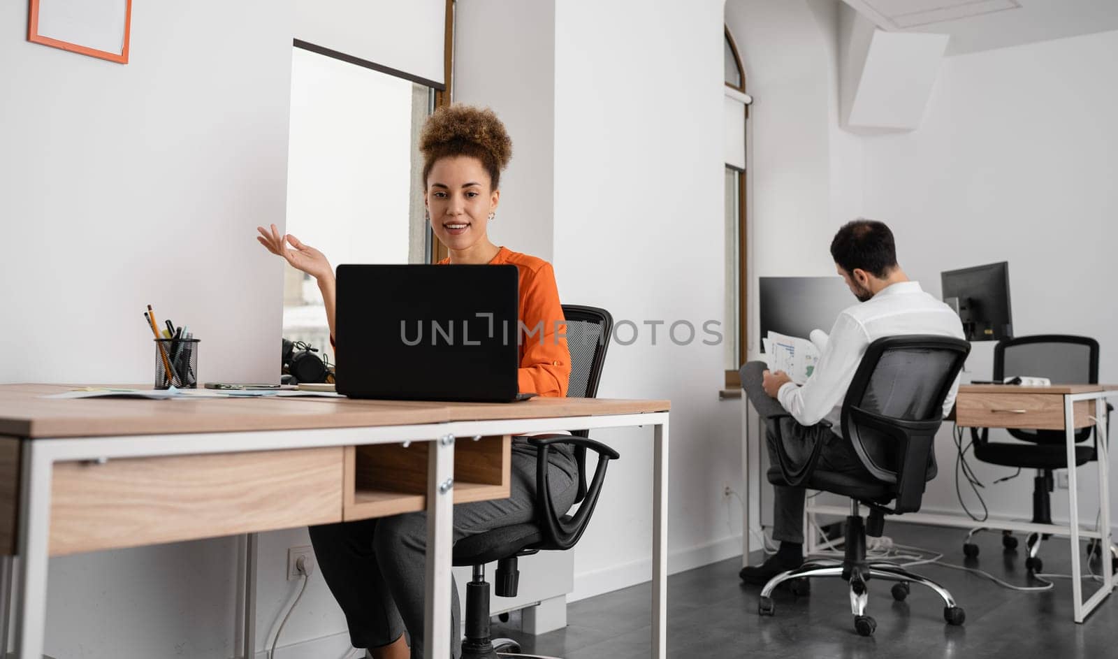 Two young businesspeople smiling while working with wireless technology in a modern workspace.