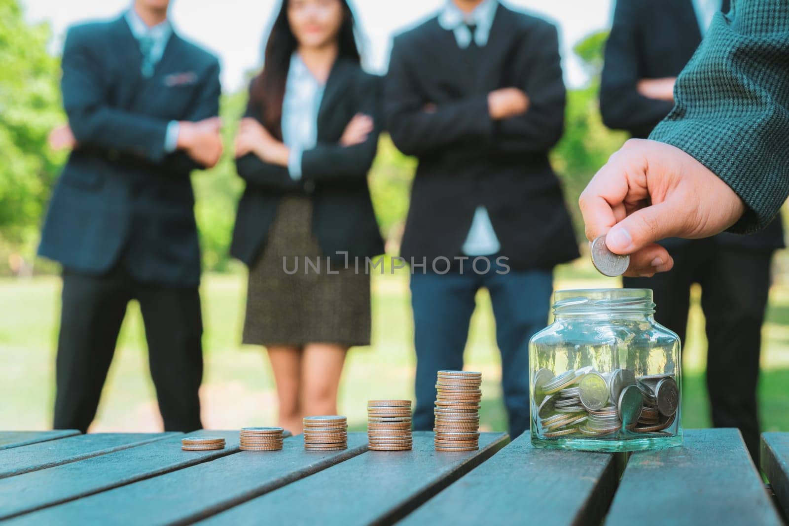 Businessman put coin to money saving glass jar on outdoor table with coin stack as sustainable money growth investment or eco-subsidize for corporate promoting environmental awareness. Gyre