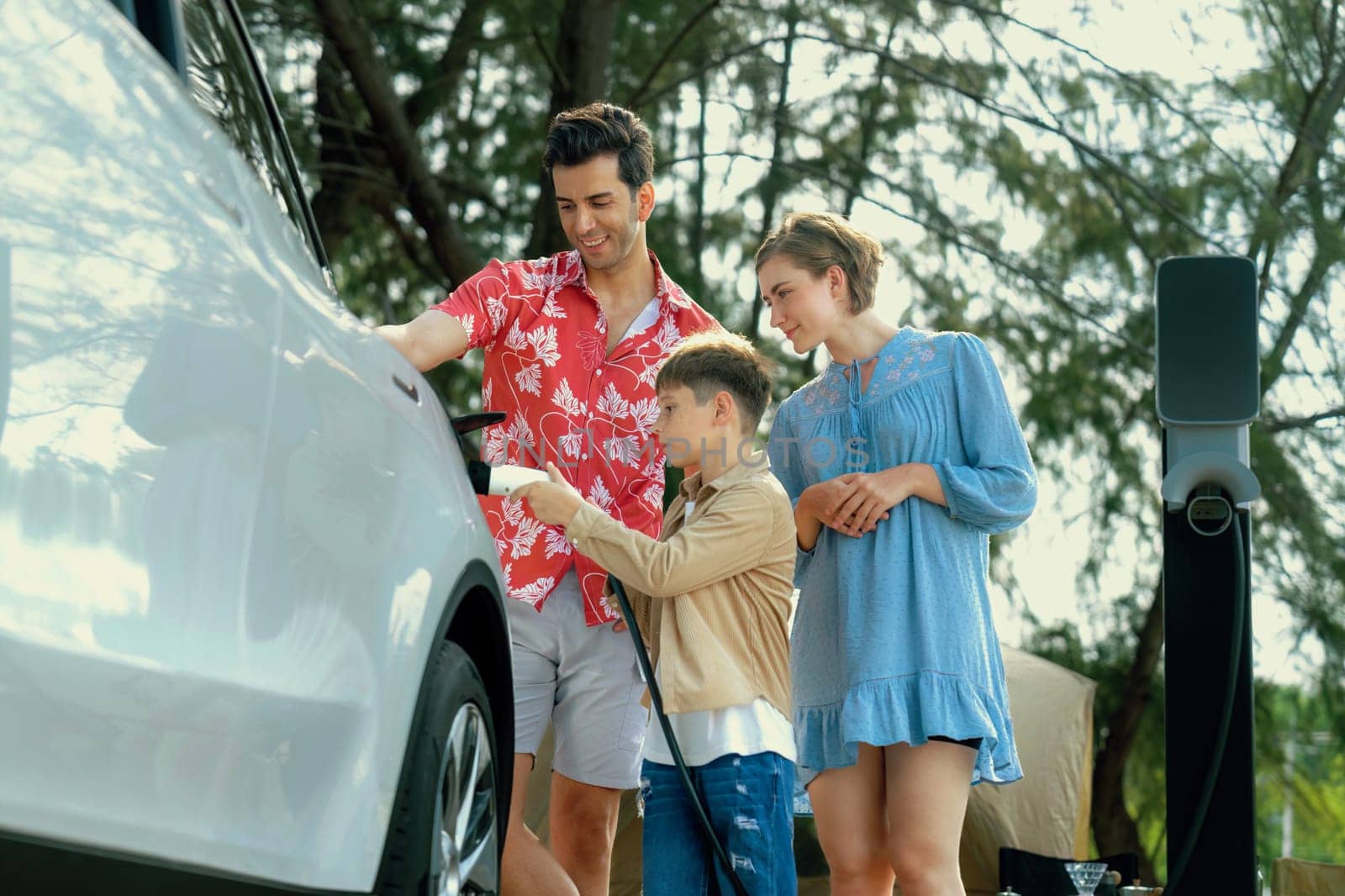 Outdoor adventure and family vacation camping in nature travel by eco friendly car for sustainable future. Lovely family recharge EV car with EV charging station in campsite. Perpetual