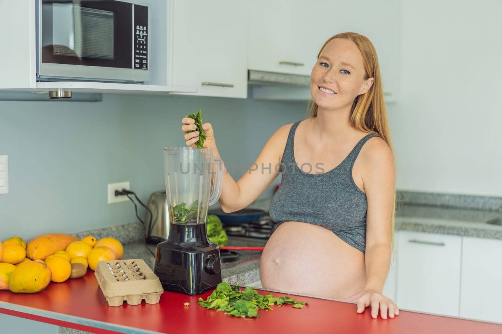 Embracing a nutritious choice, a pregnant woman joyfully prepares a vibrant vegetable smoothie, prioritizing wholesome ingredients for optimal well-being during her maternity journey by galitskaya