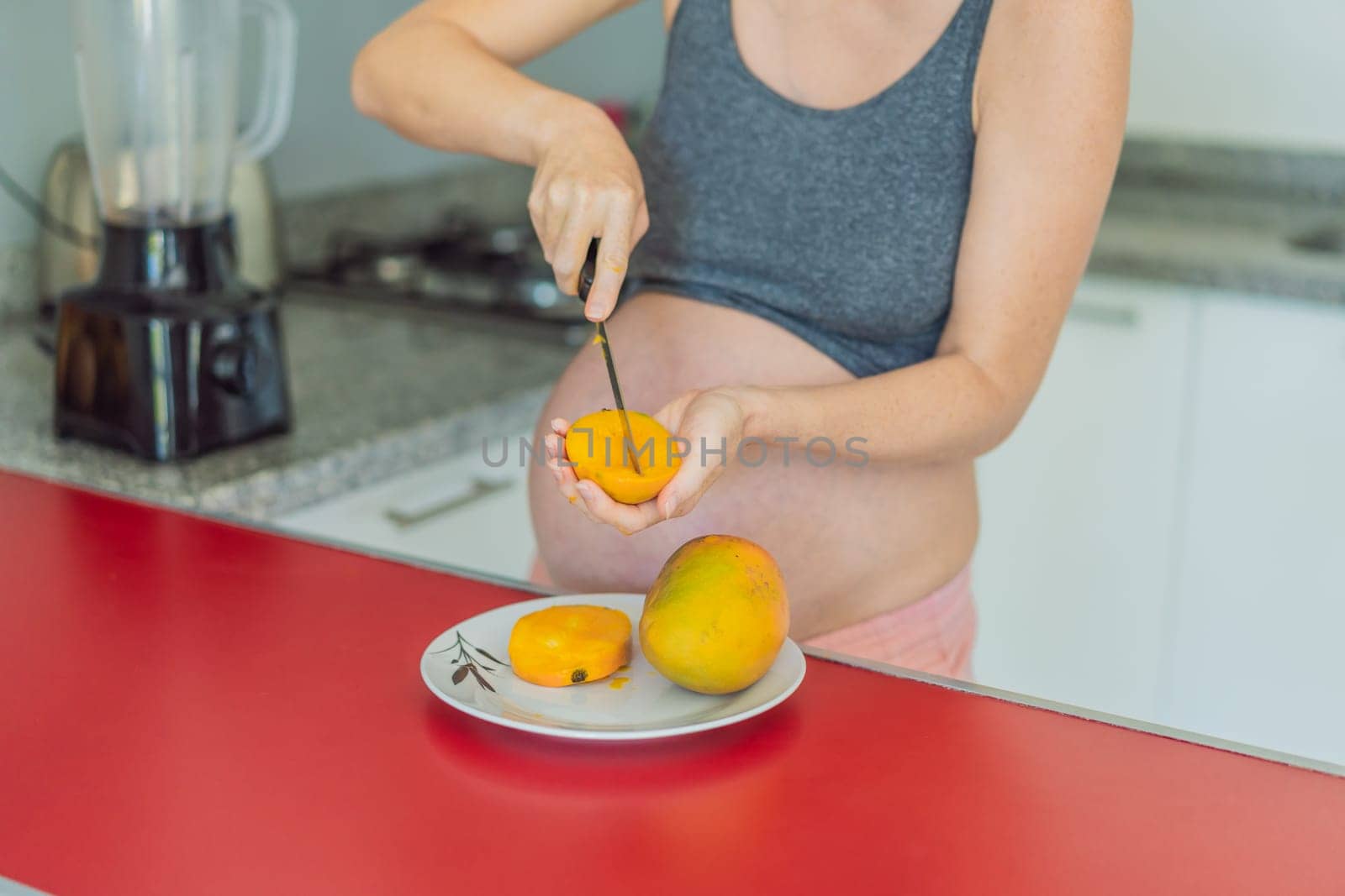 A skillful pregnant woman delicately cuts into a ripe mango, savoring a moment of culinary joy and nourishing her pregnancy with a fresh and flavorful treat by galitskaya