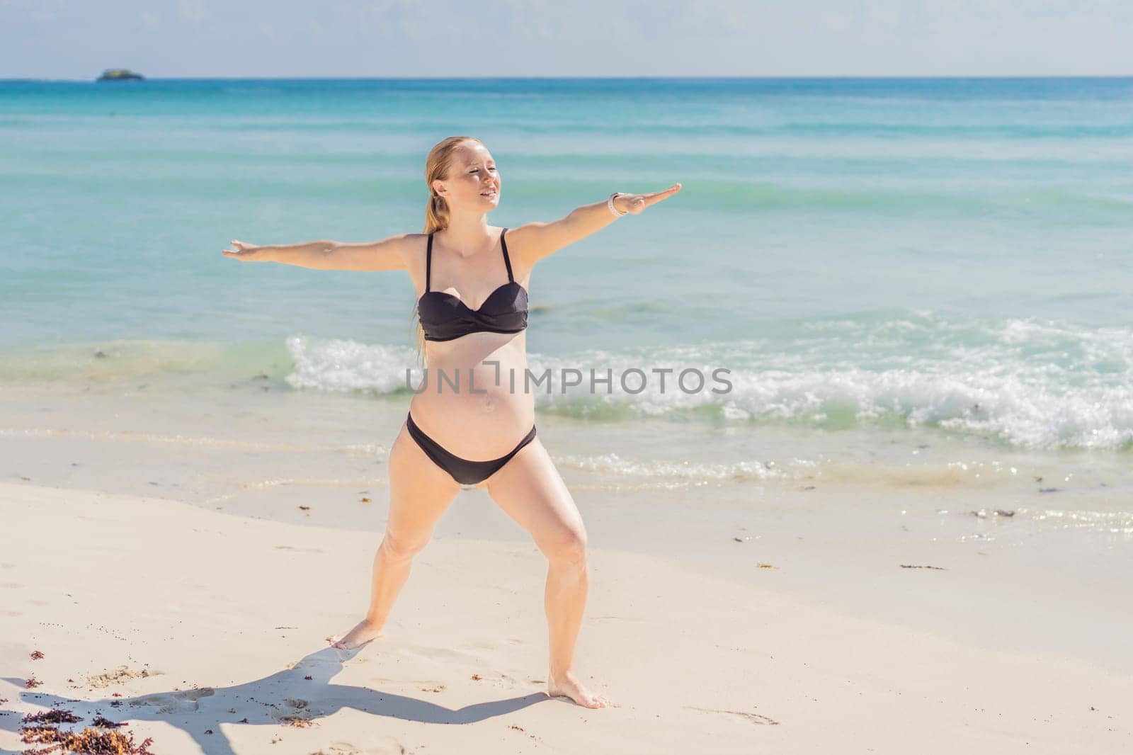 Harmonizing mind and body, a pregnant woman gracefully practices yoga on the beach, embracing the serenity of the seaside for a tranquil and mindful pregnancy experience by galitskaya