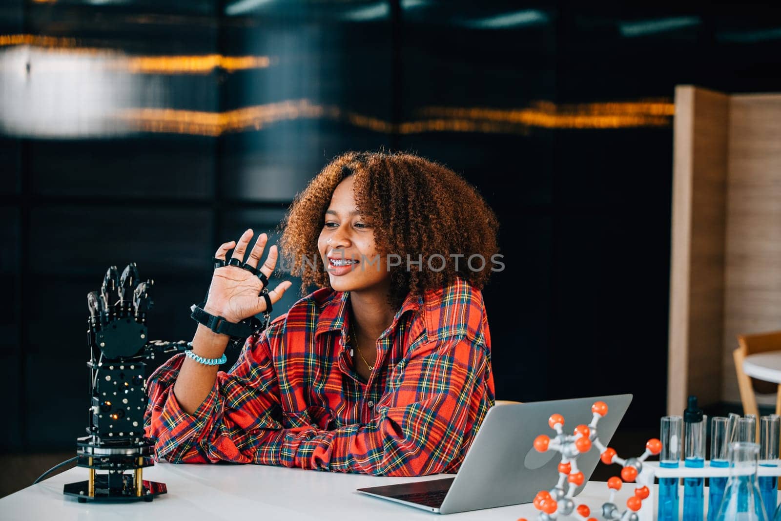 Portrait of a Black teenage student learning about a robotic arm in a classroom. She controls the arm for her engineering project showcasing intelligence and embracing technology.
