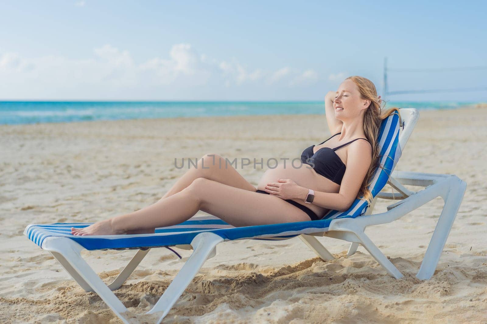 Basking in seaside tranquility, a pregnant woman lounges on a sun lounger, embracing the soothing ambiance of the beach for a moment of serene relaxation by galitskaya
