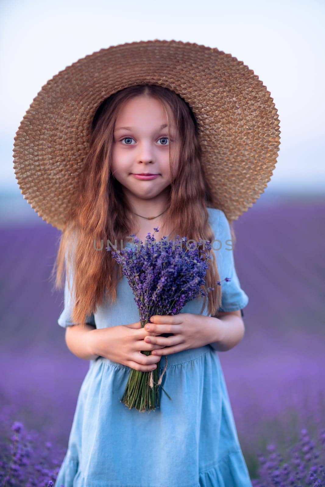 Girl lavender field in a blue dress with flowing hair in a hat stands in a lilac lavender field.