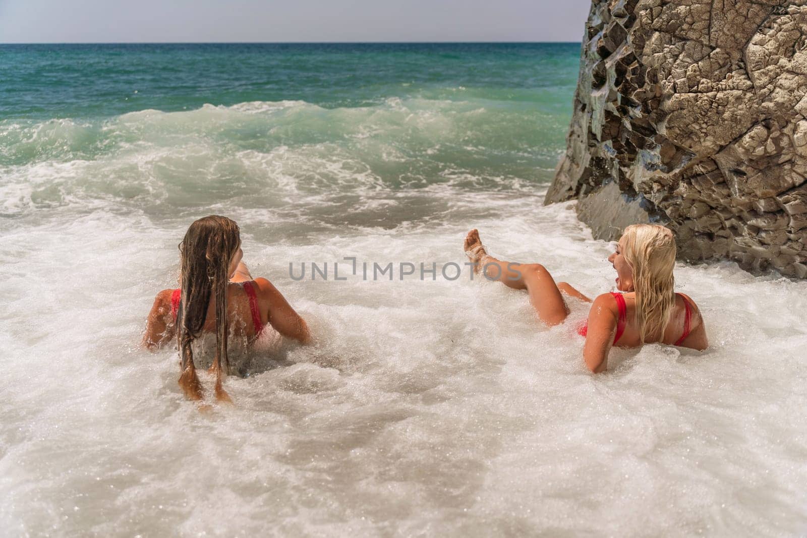 Women ocean play. Seaside, beach daytime, enjoying beach fun. Two women in red swimsuits enjoying themselves in the ocean waves. by Matiunina