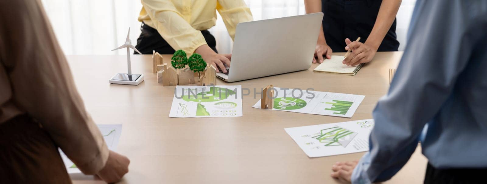 Wooden block represented green city and wind mill represented renewable energy was placed at center of green business meeting table with environmental document. Green business concept. Delineation.