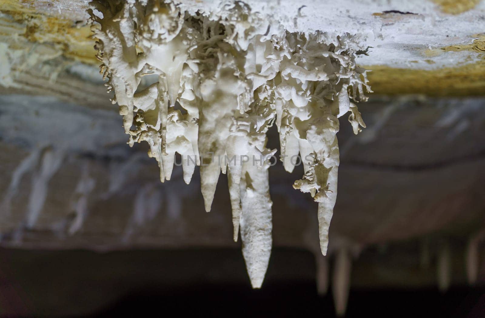 Close-up view of icicle stalactites inside a cold, dark cave in winter.