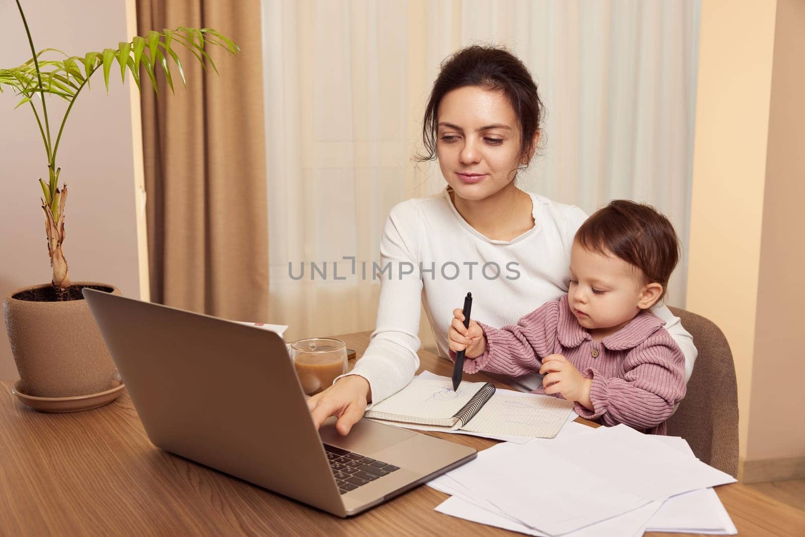 Cheerful pretty businesswoman working on laptop at home with her little child girl