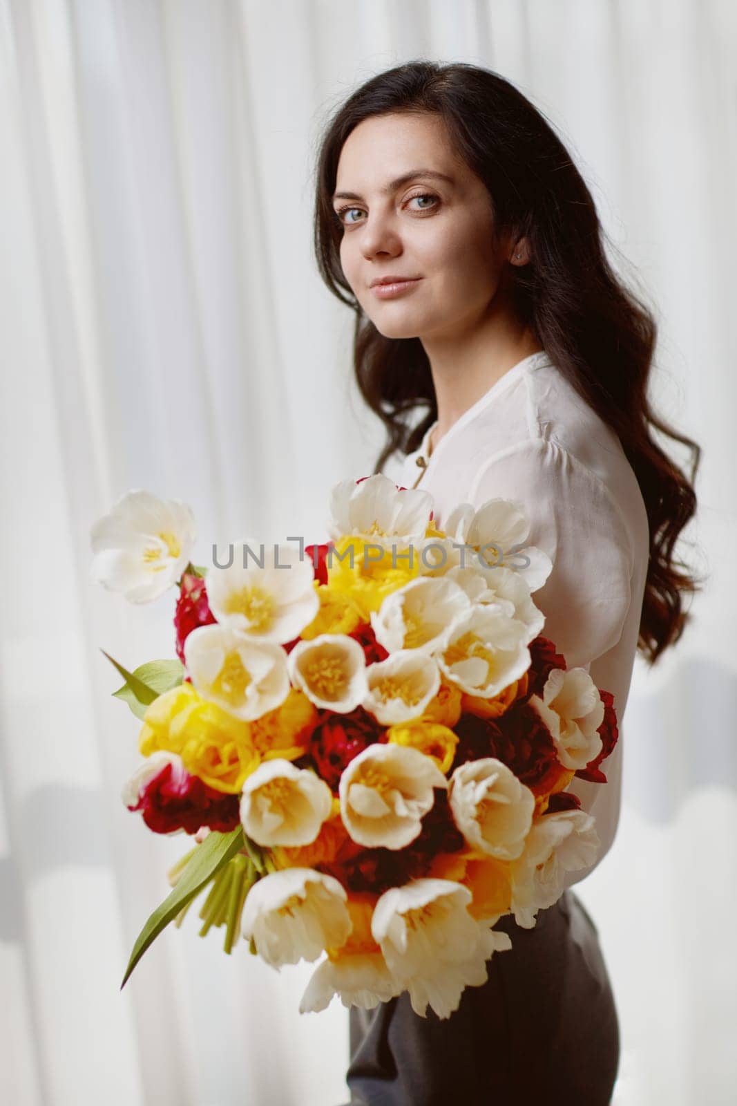 Beautiful woman in the white shirt with spring flowers tulips in hands. Women's Day