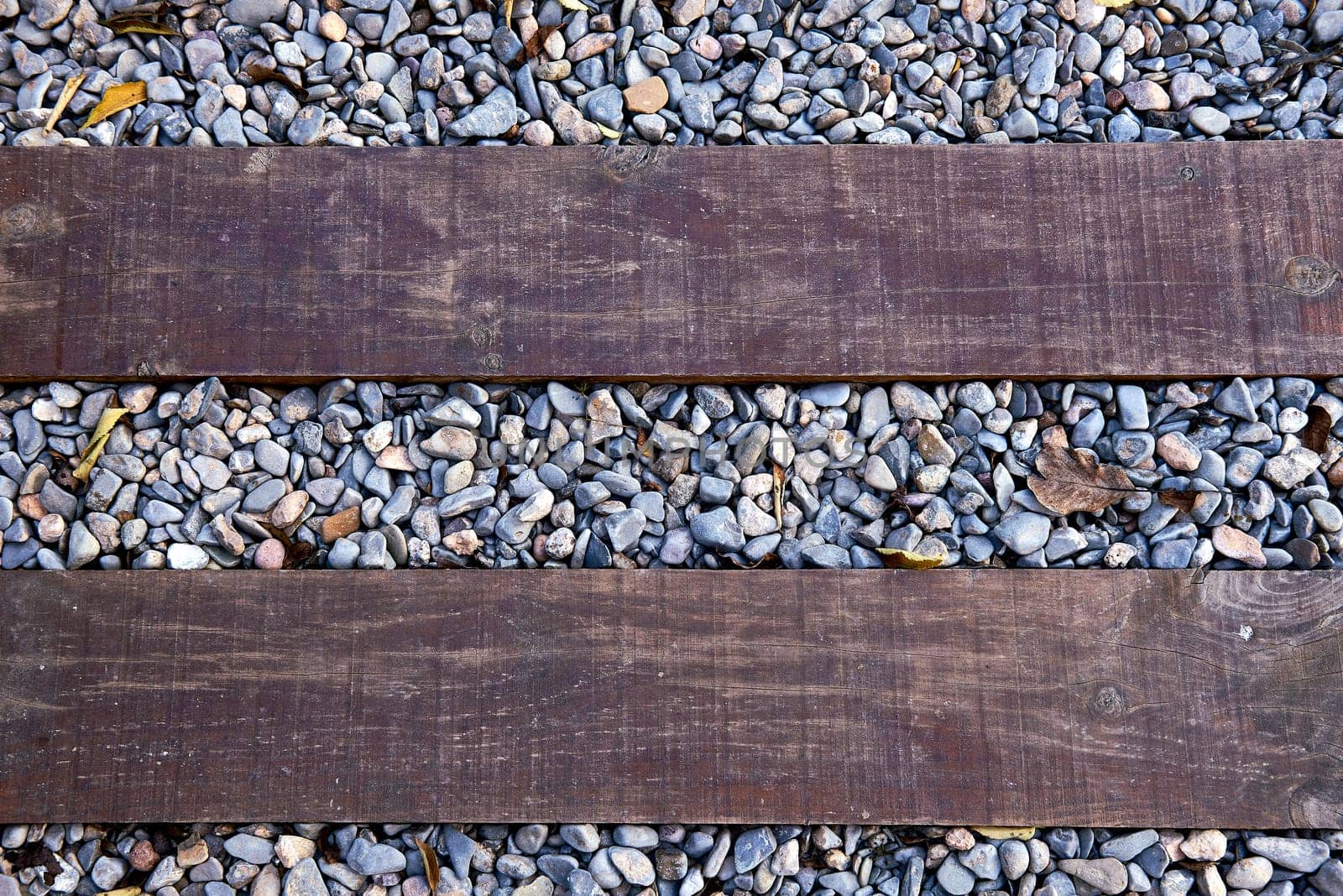 Two timbers from the side of a road on stones. Parallels, old wood, zenithal view, small stones and autumn leaves