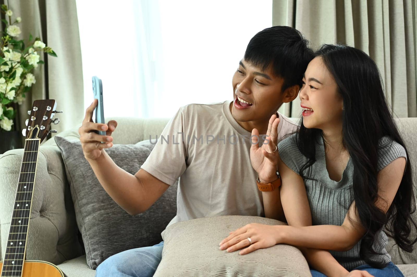 Happy young couple resting on couch taking selfies with smartphone together by prathanchorruangsak