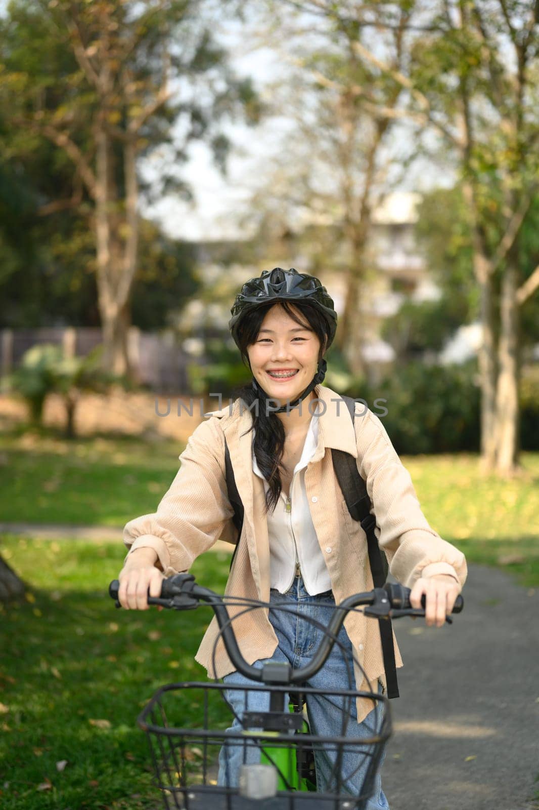 Happy smiling young female student in safety helmet riding a bicycle through the city park.