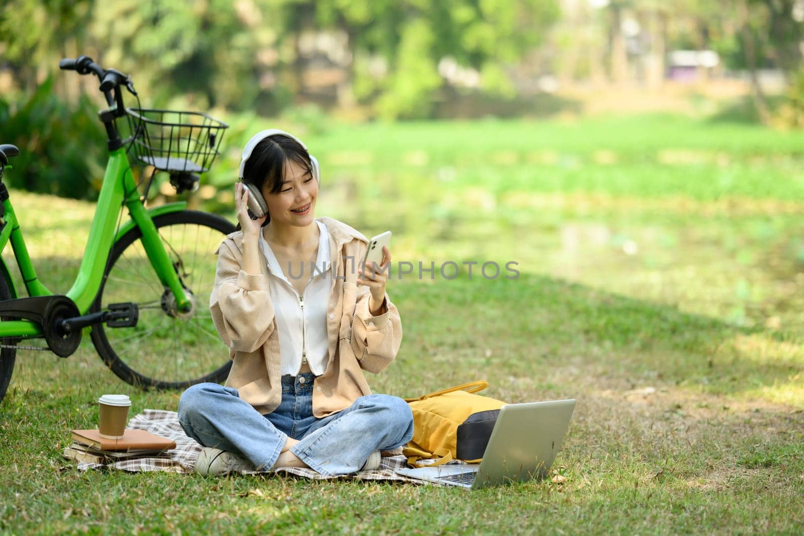 Happy young woman listening to music and using mobile phone on picnic blanket.