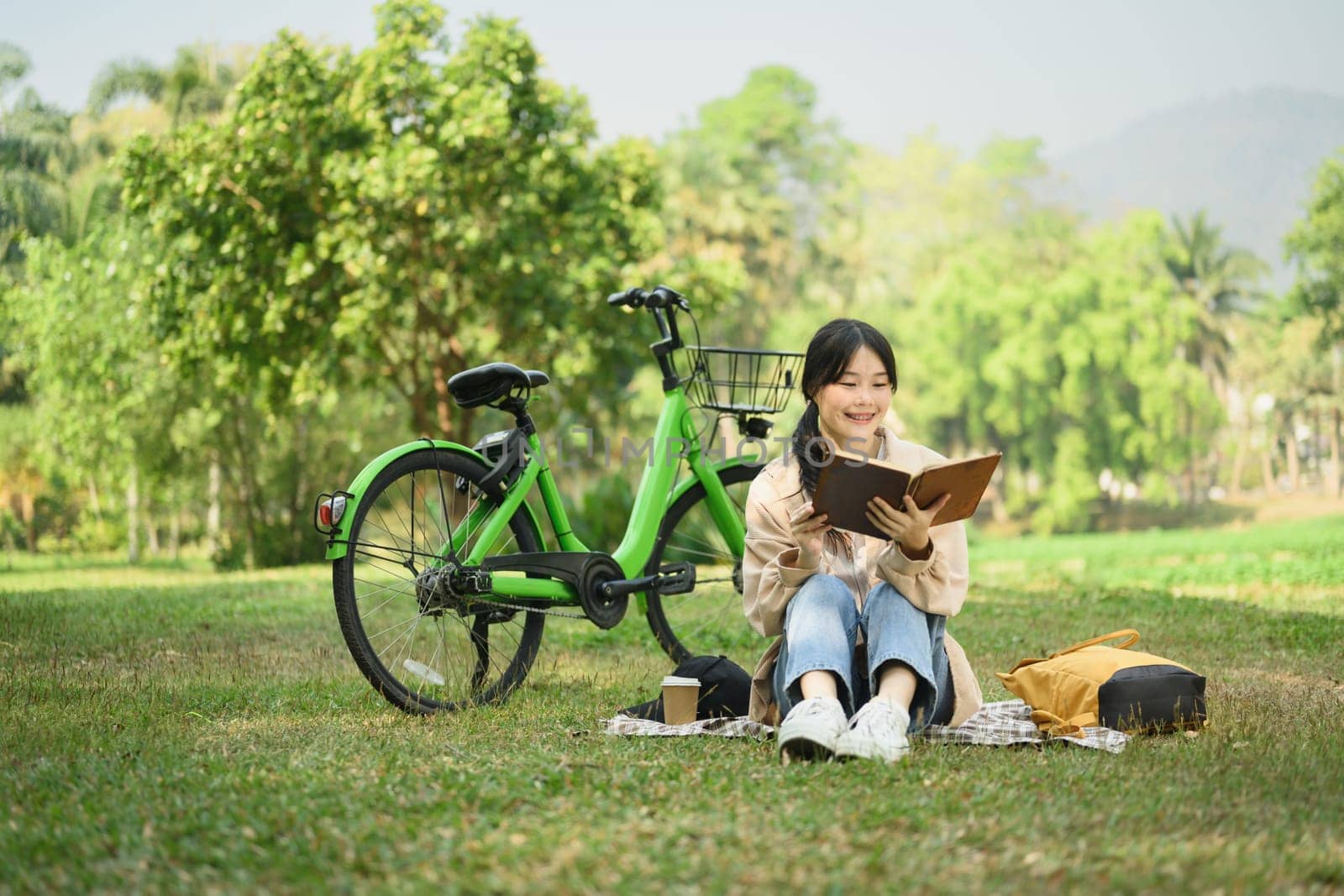Peaceful young woman relaxing on green grass and reading book during summer day.