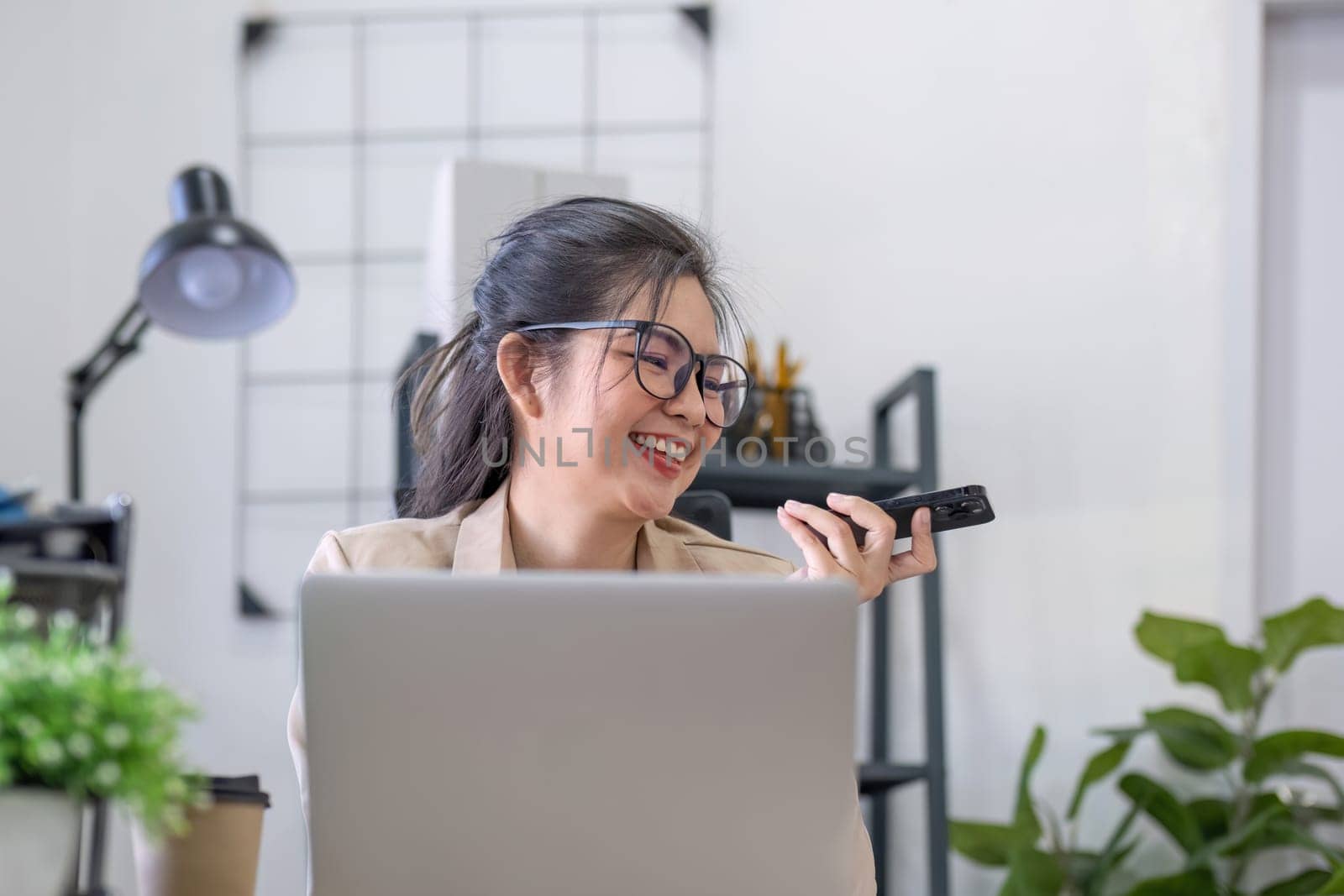 Asian businesswoman or accountant happily sitting and working with laptop on finance and business administration. On the desk in the office decorated with green plants..