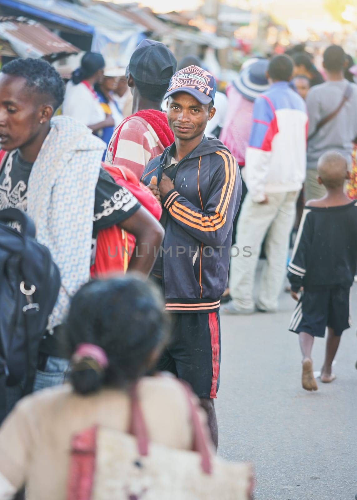 Ranohira, Madagascar - April 29, 2019: Unknown young Malagasy man standing in crowd of other blurred people on busy evening street. Madagascar people are poor but cheerful by Ivanko