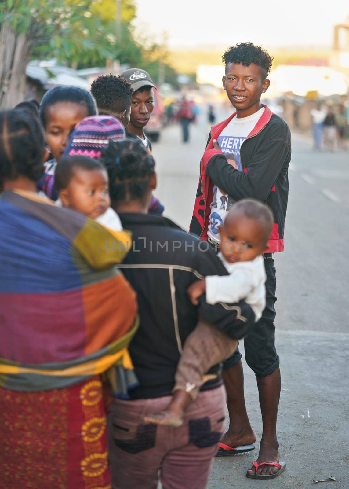 Ranohira, Madagascar - April 29, 2019: Small crowd of unknown Malagasy people standing on the main road in afternoon, one of them looking camera direction. People on Madagascar are poor but cheerful