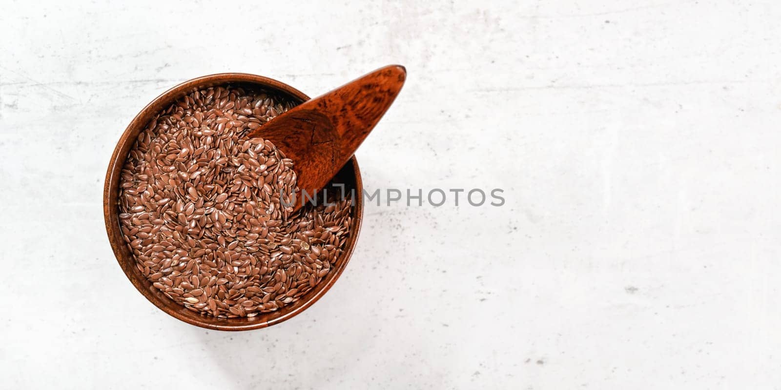 Small wooden bowl full of common flax linseed - Linum usitatissimum - little scoop inside, on white stone like desk, view from above, space for text right side by Ivanko