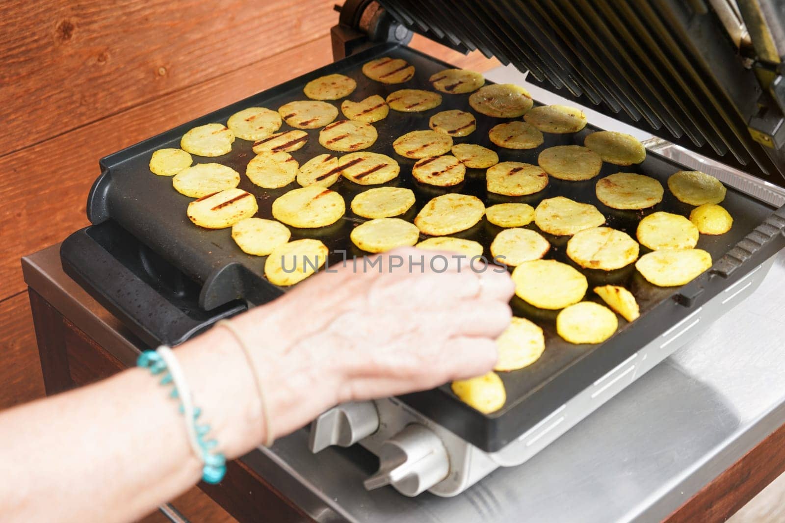 Potatoes cut to small pieces grilled on electric grill, blurred senior hand over them as they're getting moved over by Ivanko