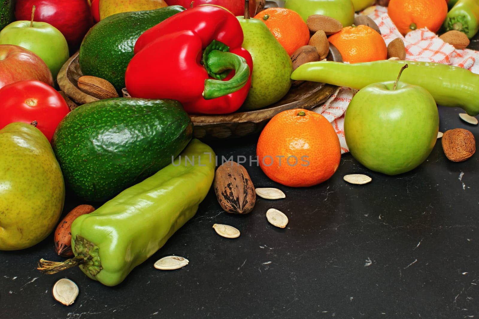 Mixed fruits and vegetables - red peppers, avocado, apples, pears, tangerines, pecan nuts, almonds and pumpkin seeds on wooden bowl, close up view