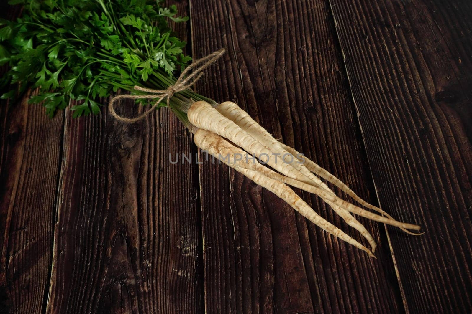 Bunch of parsley / parsnip roots with green leaves lying on dark wooden rustic board
